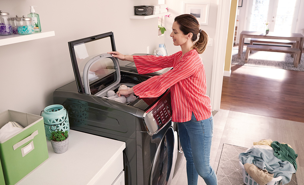 A woman putting laundry into a top-load high-efficiency washing machine.