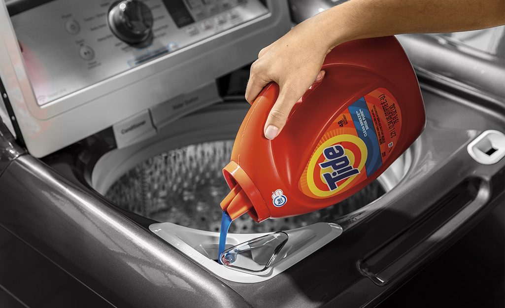 Someone pours high-efficiency laundry detergent into an HE washer.