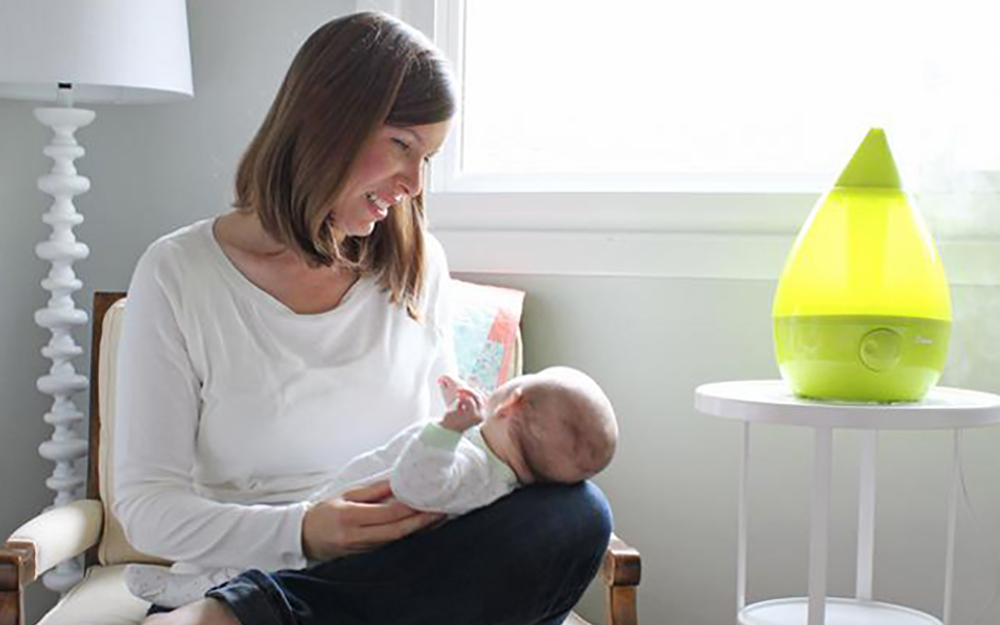 A woman holding a baby uses a humidifier in a nursery.