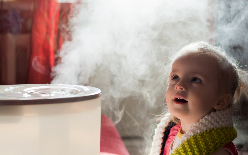 A little girl looks at the steam coming from a humidifier.