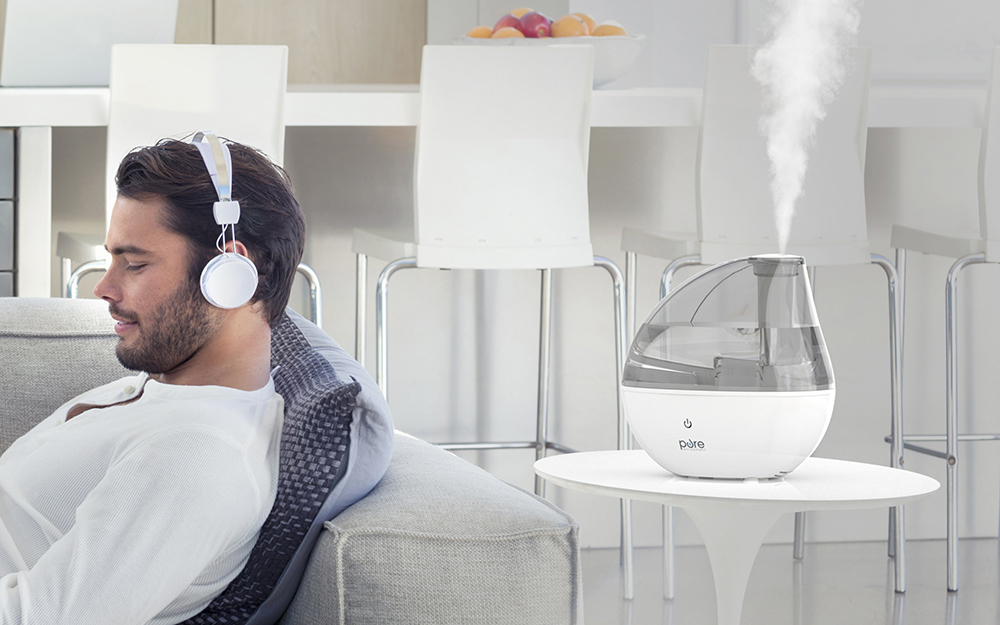 A man relaxes on his couch with a humidifier on a table behind him.