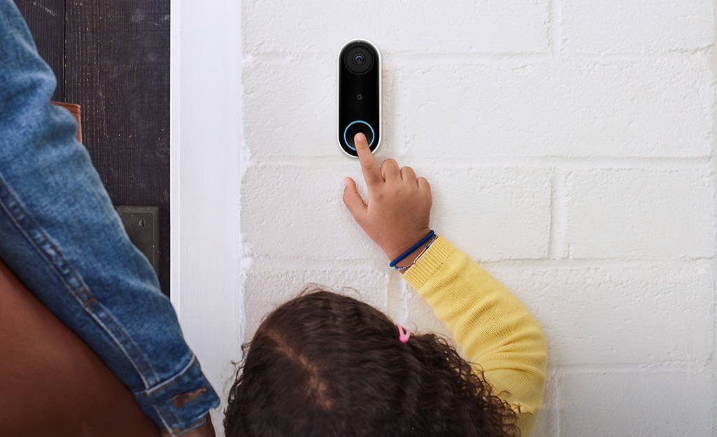 A child reaches up to press the button to activate the intercom on a smart doorbell.