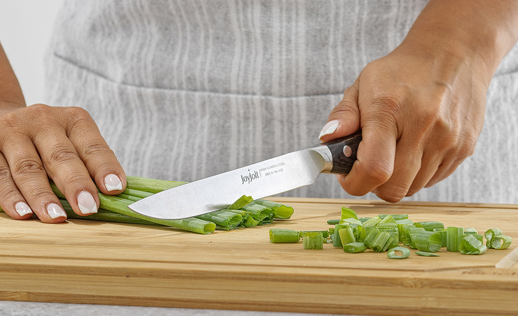 A person using a knife to cut scallions on a wood cutting board.