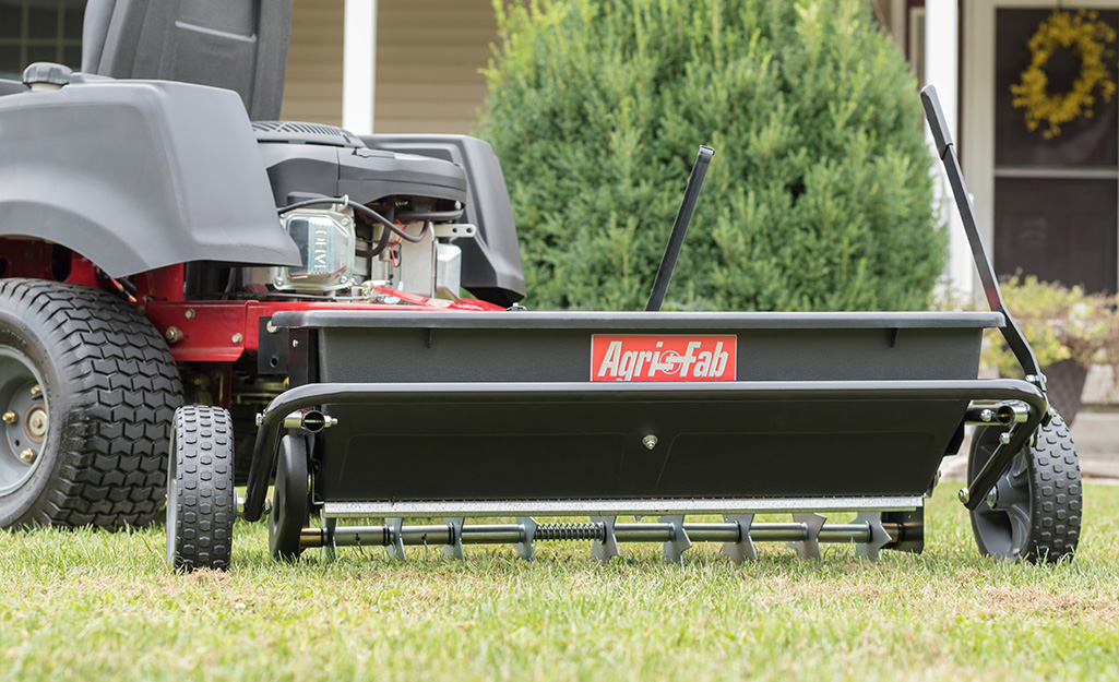 A garden tractor pulling a spiker seed drop spreader over a lawn. A garden tractor pulling a spiker seed drop spreader over a lawn.