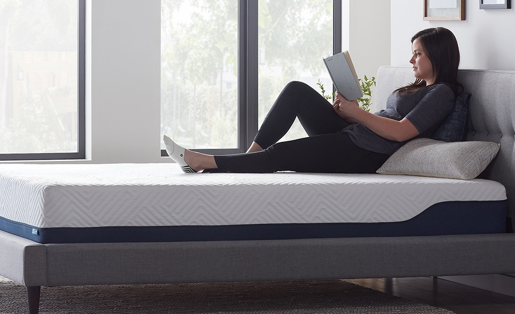 A woman reading on a bed with an uncovered memory foam mattress.