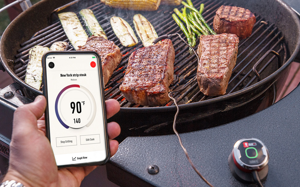 A wireless digital meat thermometer displays the temperature of grilled meat on a smart phone.