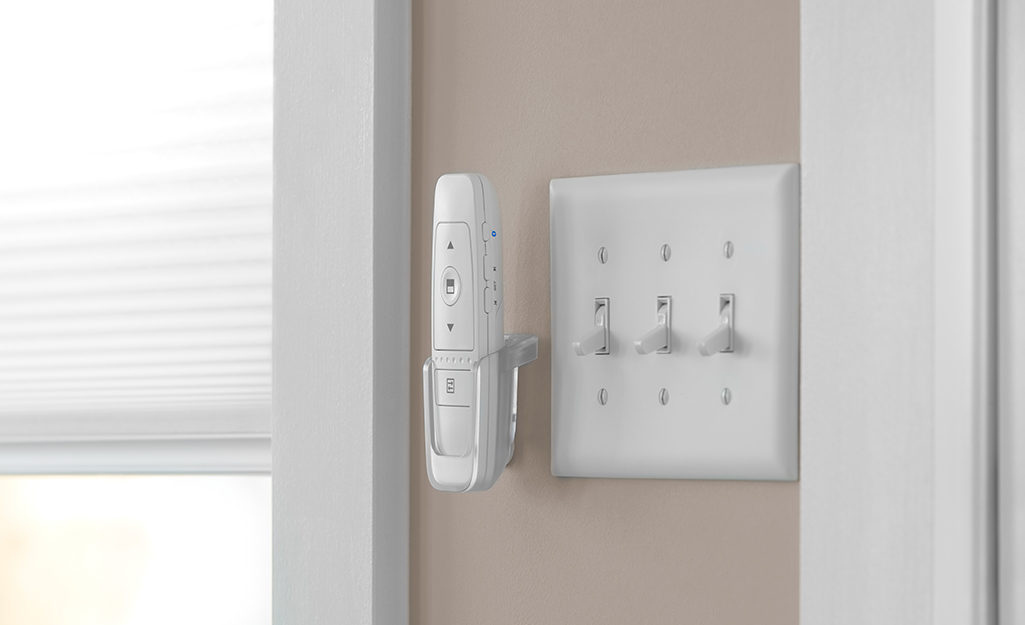 A motorized blind remote hangs on the wall between the window and light switch.