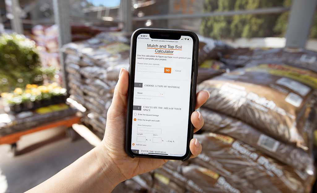 A person holds up a smartphone with The Home Depot mulch calculator on the screen.