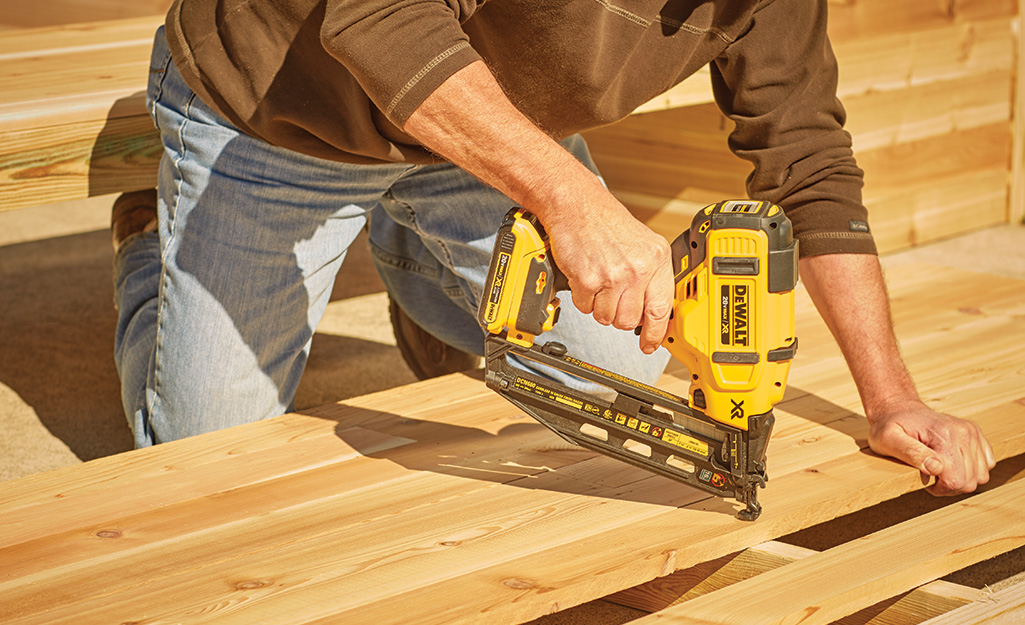 A man nailing boards with a cordless electric nail gun.