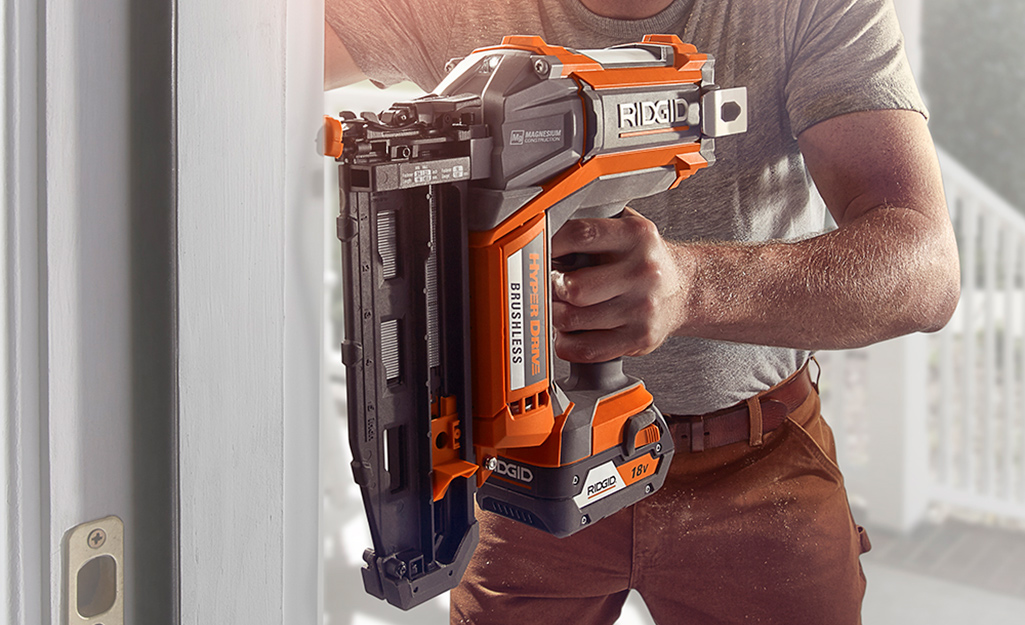 A person using a 15-degree nail gun against a door frame.