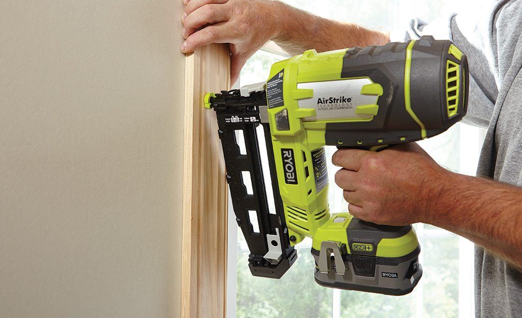 A man nailing trim to a wall with a cordless electric nail gun.