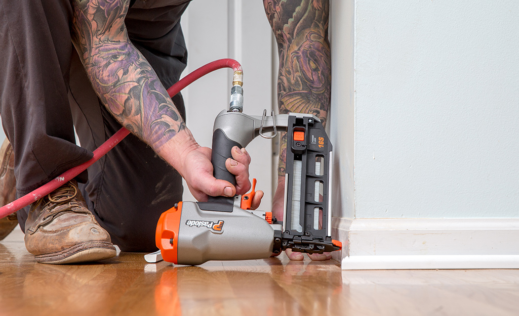 A person nailing moulding using a pneumatic nail gun.