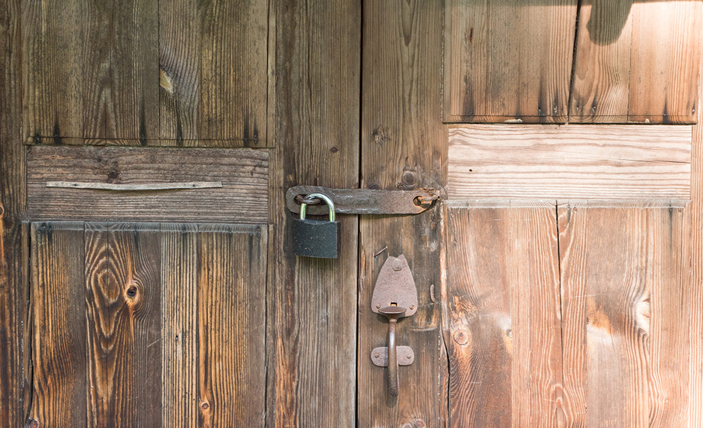 A warded padlock on a weathered barn door.