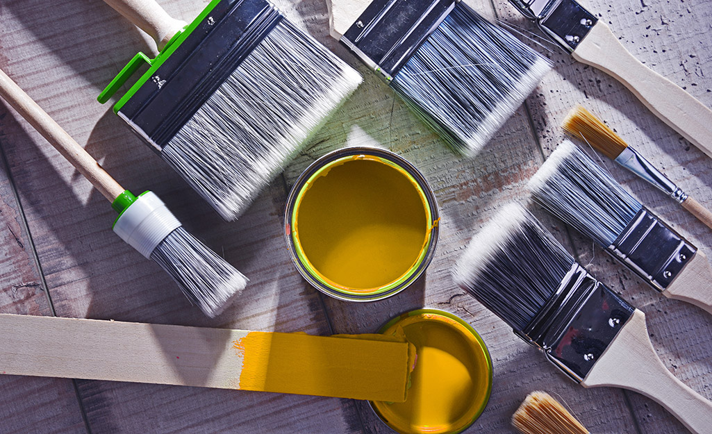 Paint brushes of different sizes arranged around a can of yellow paint.