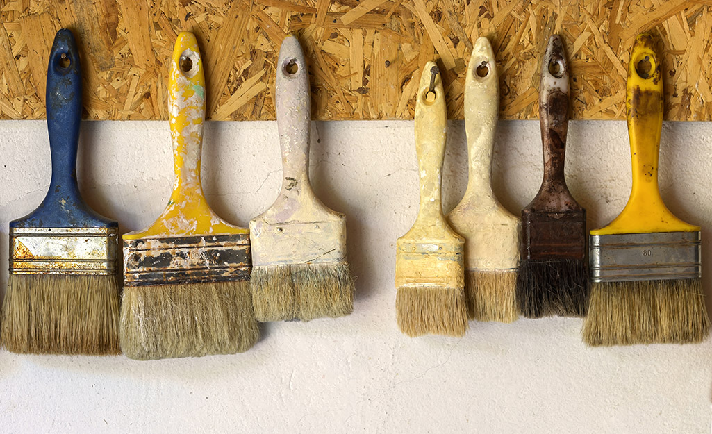 Paint brushes hanging on hooks for storage on a wall.