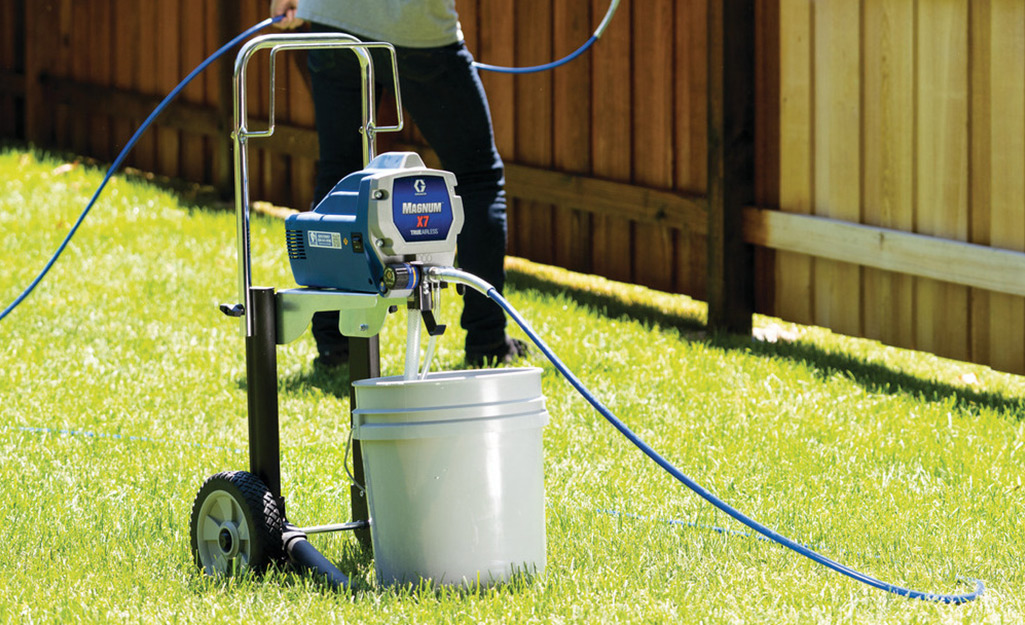 A person uses a paint sprayer to add stain to a wooden fence.