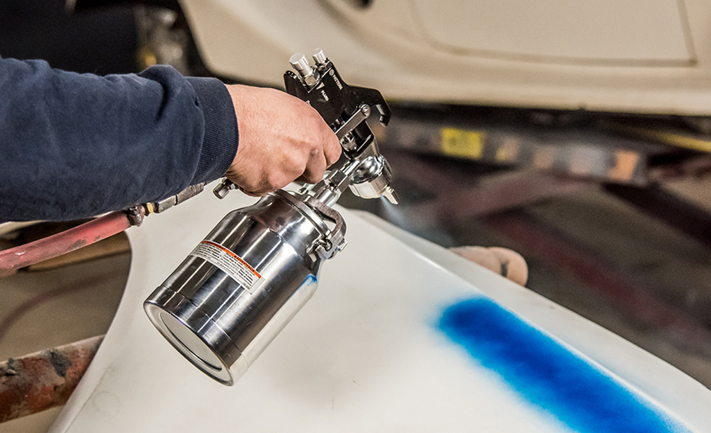 A person uses a compressed air paint sprayer to paint a blue line.