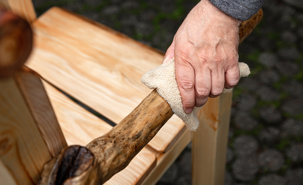 A person uses a rag to wipe off the arm of a wooden chair.