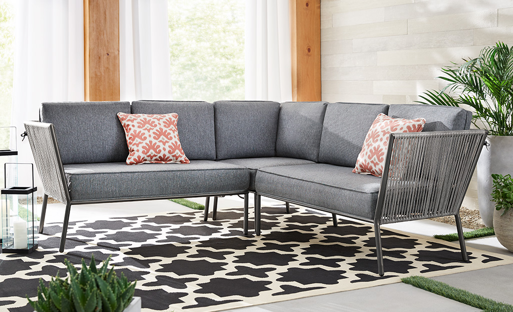 Gray sectional sofa with red patterned pillows on a patio.