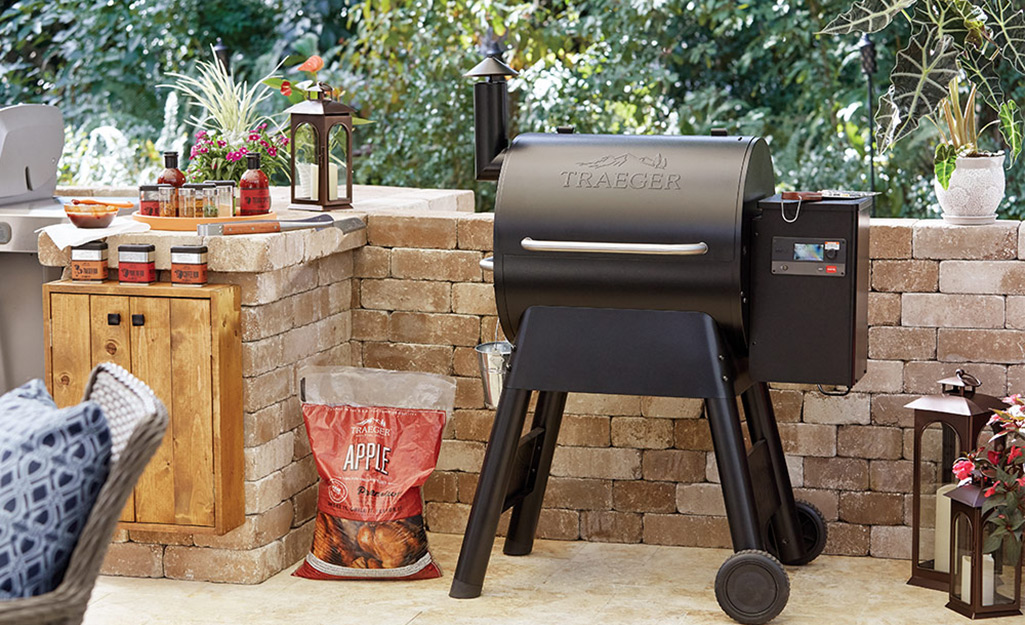 A bag of apple wood pellets for smoking sits next to a pellet grill on a stone patio. 