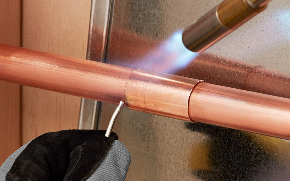 A propane torch solders copper pipe.