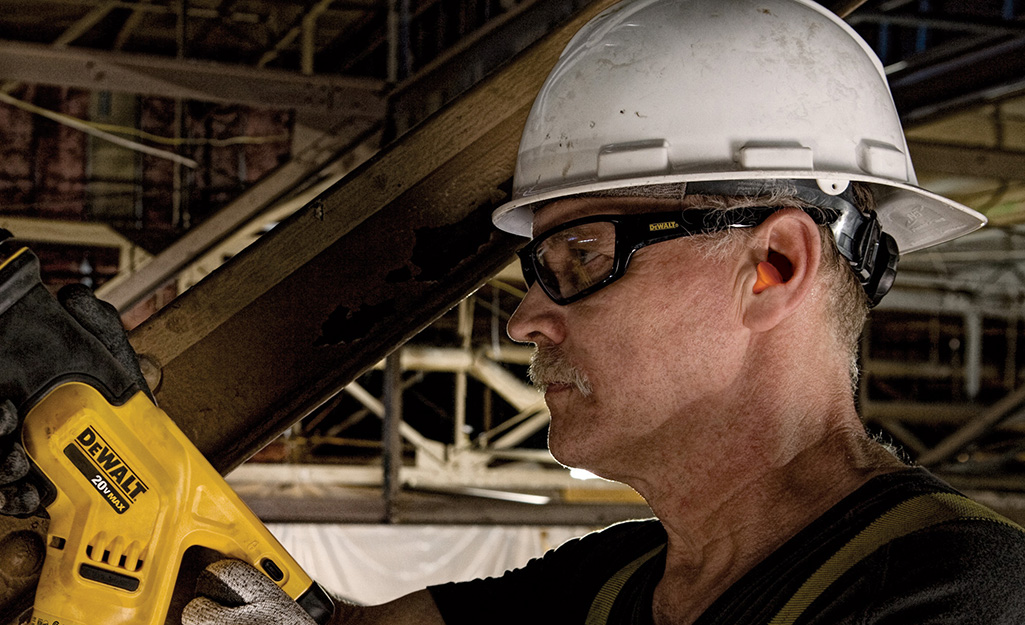 A man wearing safety glasses and a hard hat while using a power tool.