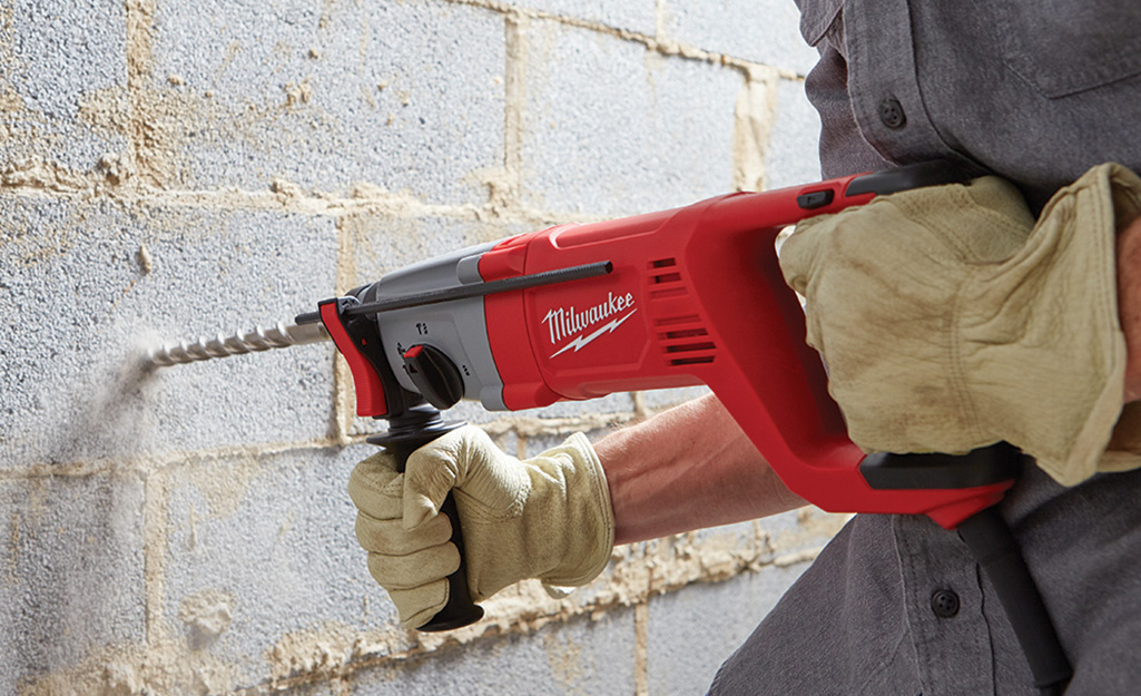 A person using a hammer drill to drill a concrete wall.