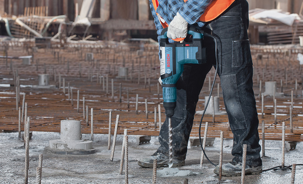 A person using a rotary hammer drill to set into a foundation.