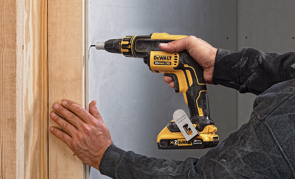 A person using a screw gun on a wooden frame against a wall.