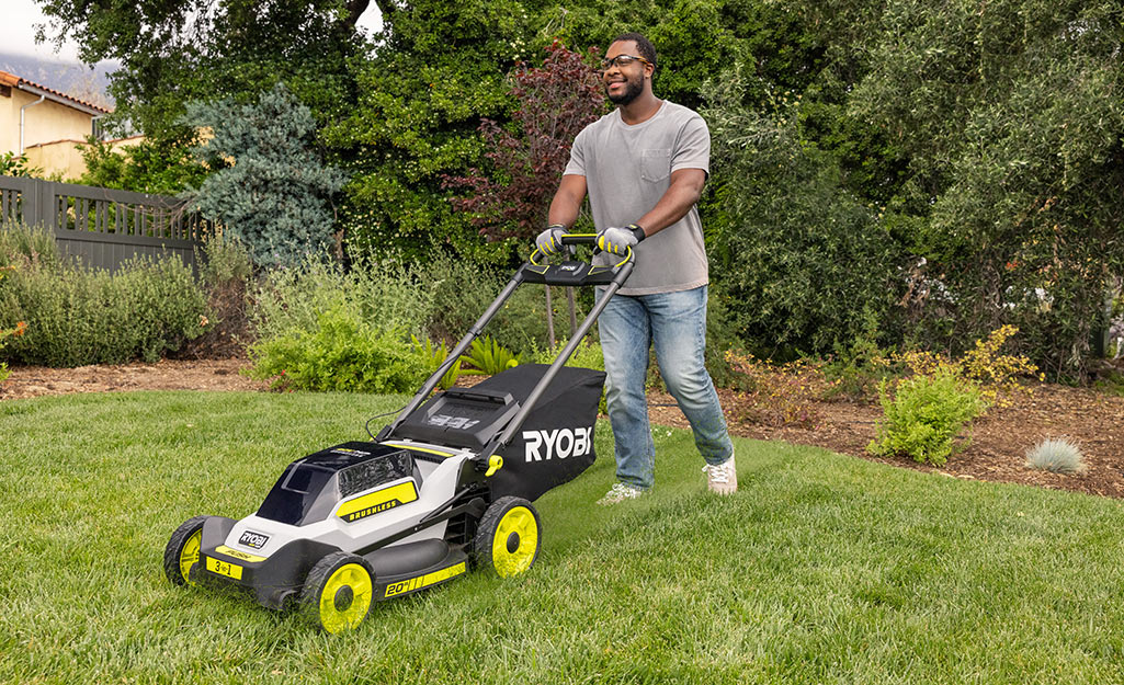A man uses a push mower in his front yard. 