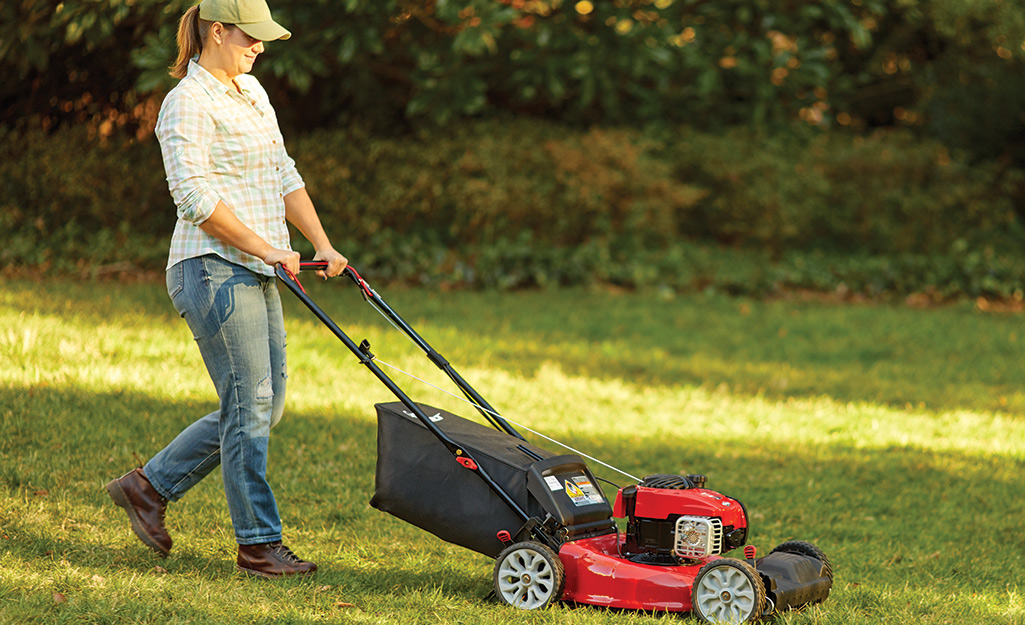 A woman uses a gas push mower. 