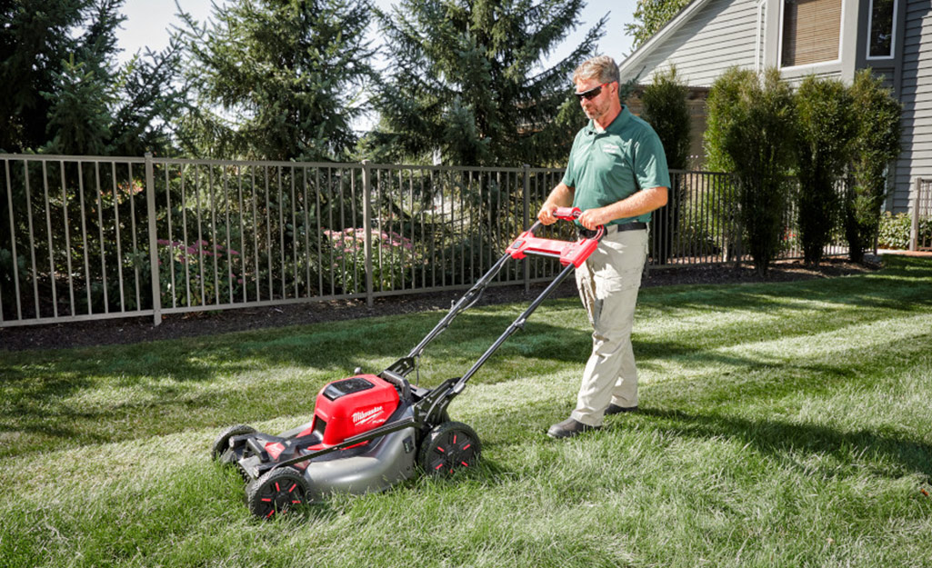 A man mowing a flat lawn with a push mower. 