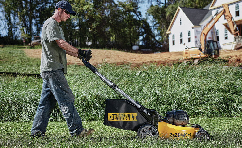 A man uses a push mower that automatically collects clippings. A man uses a push mower that automatically collects clippings.