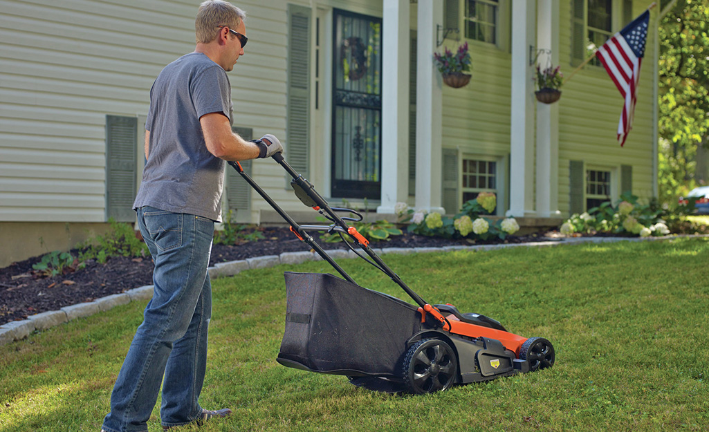 A man uses a high-wheel push mower. A man uses a high-wheel push mower.