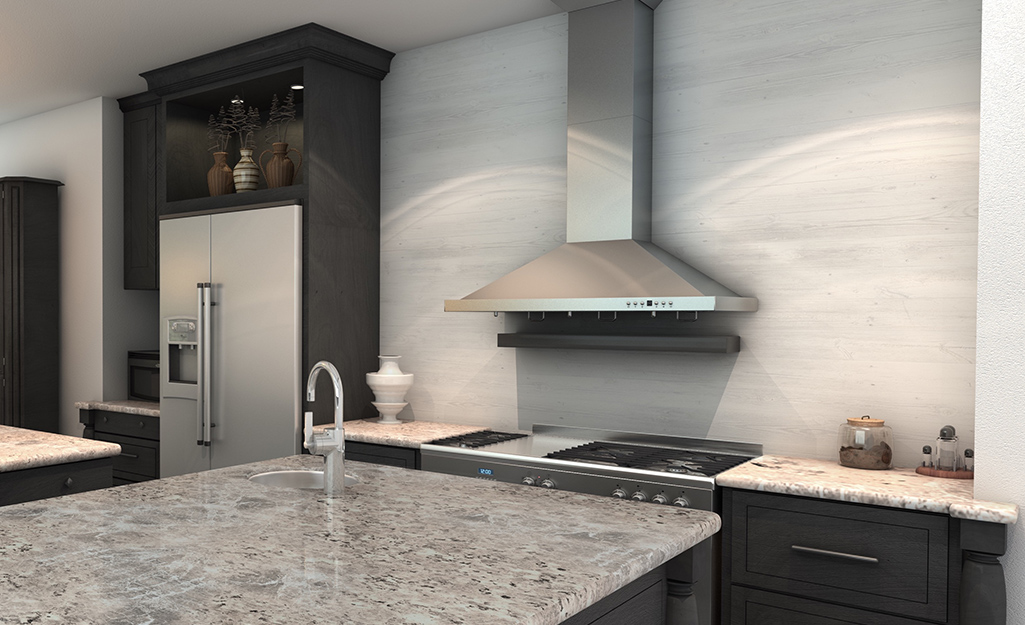 A stainless steel wall-mounted range hood in a kitchen with a marble-look wall.