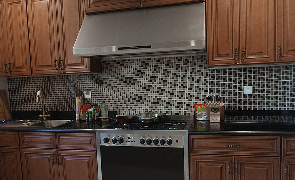 A stainless steel under-the-cabinet range hood in a kitchen with wooden cabinets.