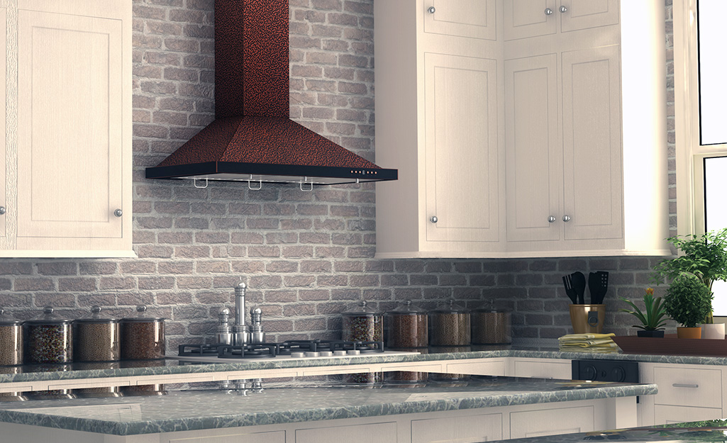 A copper range hood mounted on a brick wall in a kitchen.