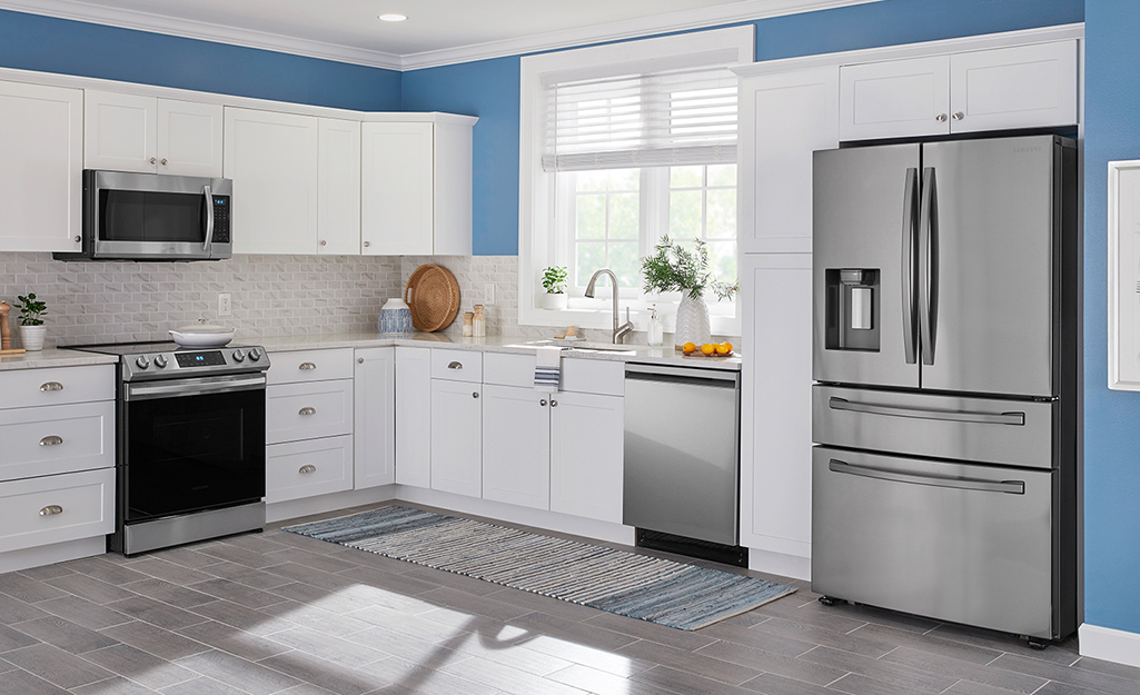 A stainless steel French door refrigerator stands in a white and blue kitchen.