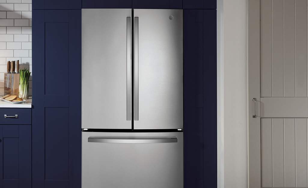 A stainless steel energy-efficient refrigerator flush with blue cabinets.