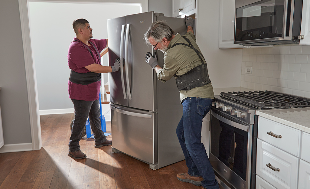 Two people installing a refrigerator in a kitchen.