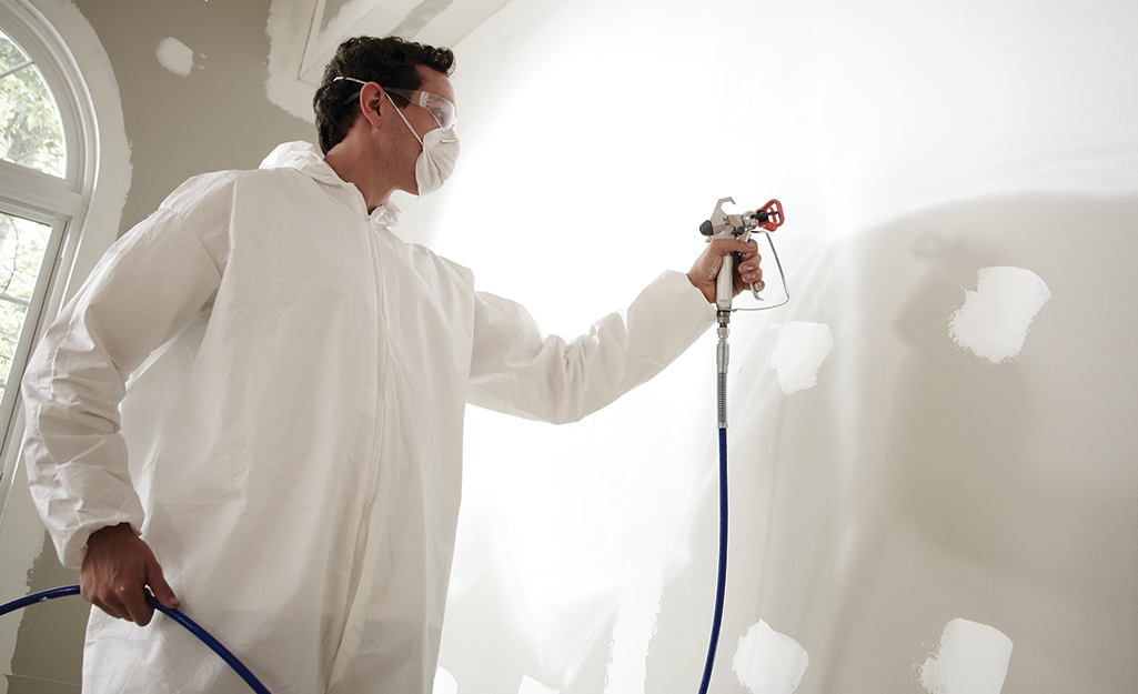 A person in protective paint gear using a paint sprayer.