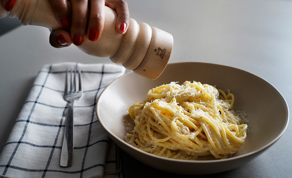 A woman uses a pepper mill to add flavor to her pasta. 