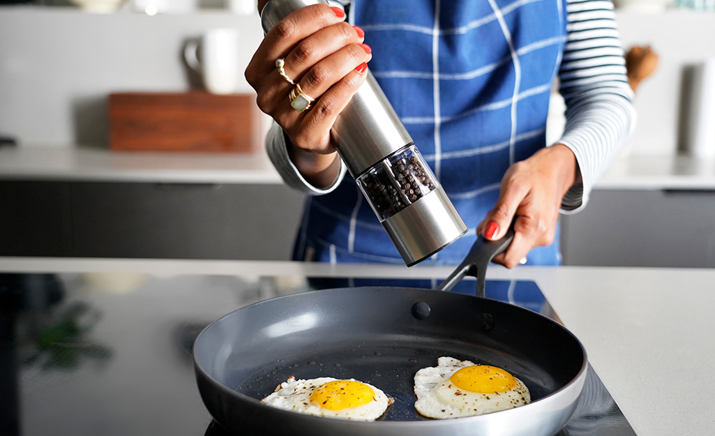 A woman uses a stainless steel pepper grinder to season eggs. 