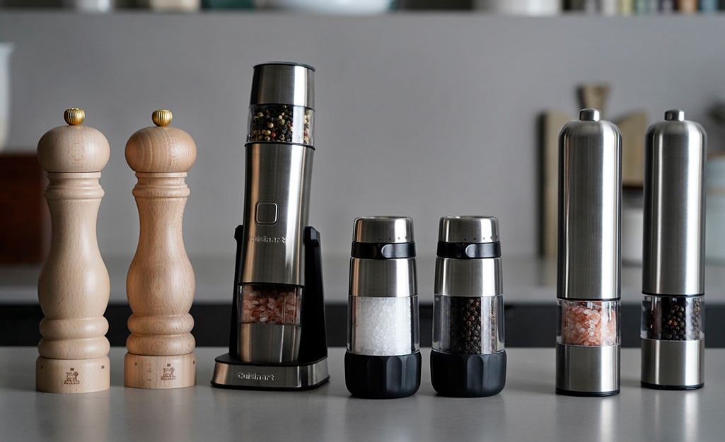 A variety of salt and pepper grinders are displayed on a counter. 