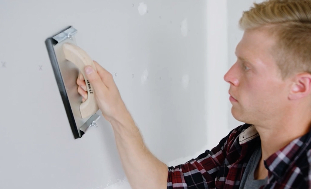 A person using a hand sander to smooth drywall.