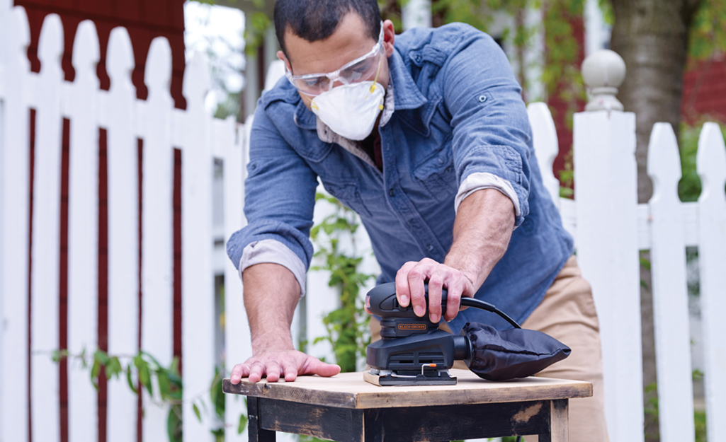 A person using a power sander outdoors on a wood project.