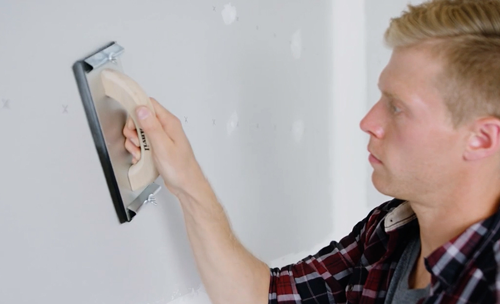 A person using a hand sander to smooth drywall. A person using a hand sander to smooth drywall.