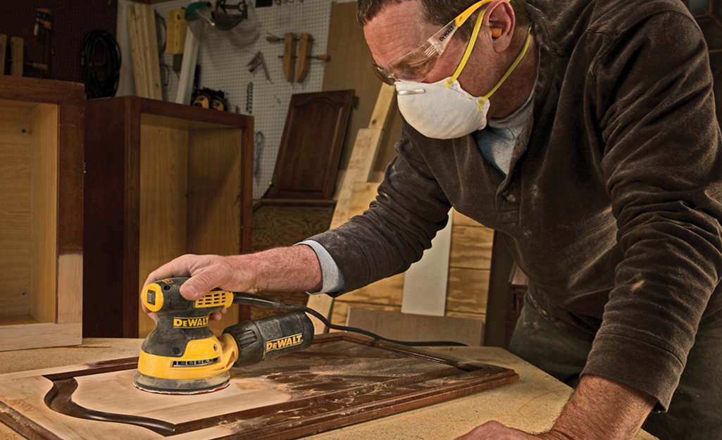 A person in a face mask using a sander.
