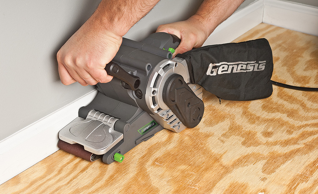 A person using a sander on a plywood floor.