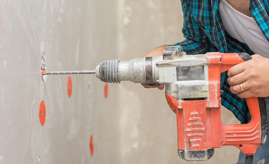 A person drilling into unfinished drywall.